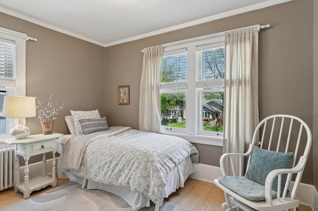bedroom featuring wood finished floors, crown molding, radiator heating unit, and baseboards