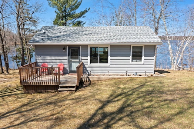 view of front facade featuring roof with shingles, a wooden deck, and a front lawn