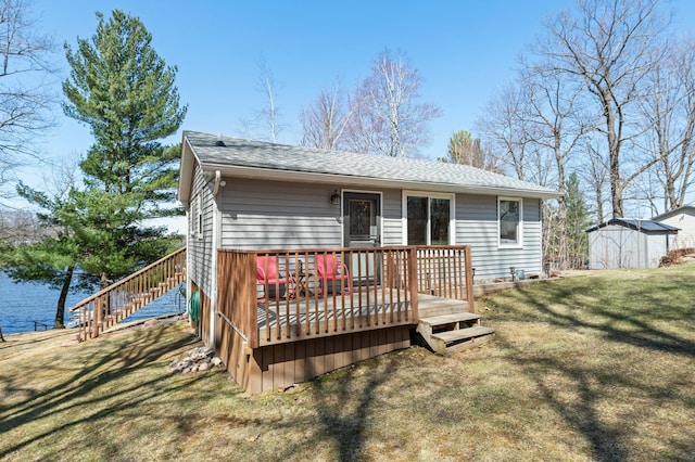 rear view of property featuring an outdoor structure, a wooden deck, roof with shingles, a storage unit, and a yard