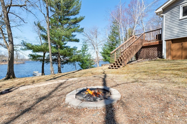 view of yard with a deck with water view, stairs, and an outdoor fire pit