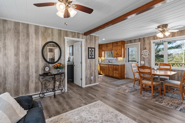 dining area with wooden walls, ceiling fan, wood finished floors, and beam ceiling