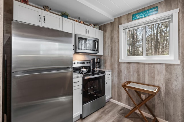 kitchen featuring baseboards, white cabinets, light stone counters, light wood-style flooring, and appliances with stainless steel finishes
