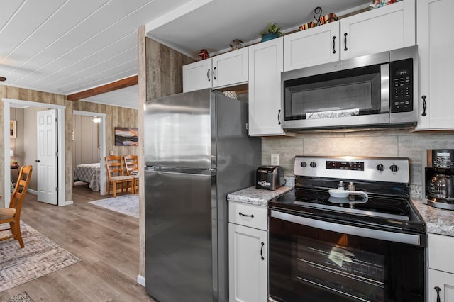 kitchen with wood walls, white cabinetry, light wood finished floors, backsplash, and stainless steel appliances