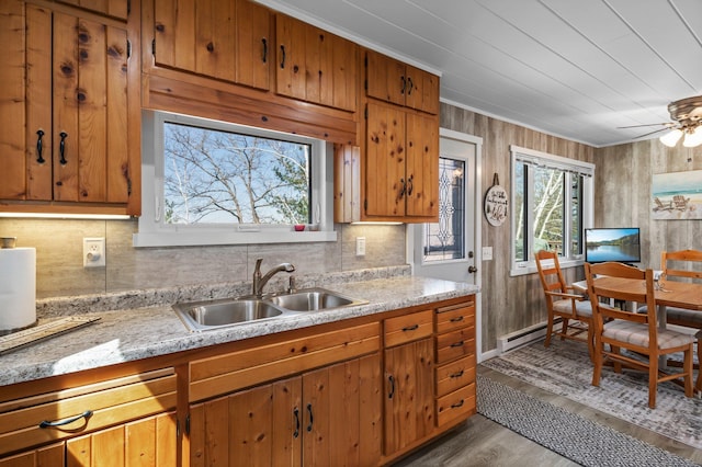 kitchen featuring decorative backsplash, a ceiling fan, brown cabinets, wood finished floors, and a sink