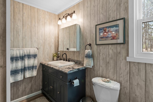 half bath featuring vanity, wood walls, and toilet