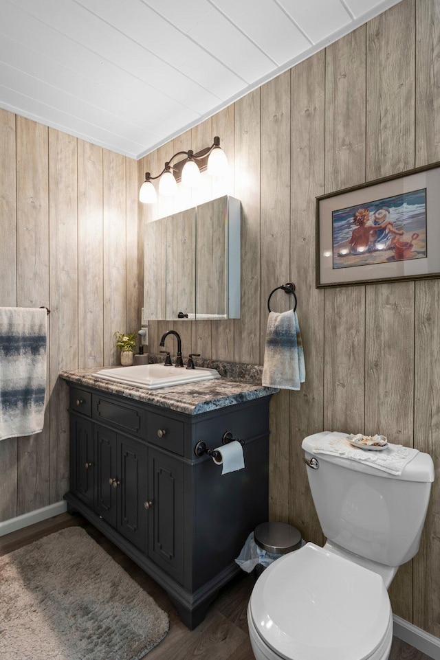 bathroom with wood walls, vanity, toilet, and wood finished floors