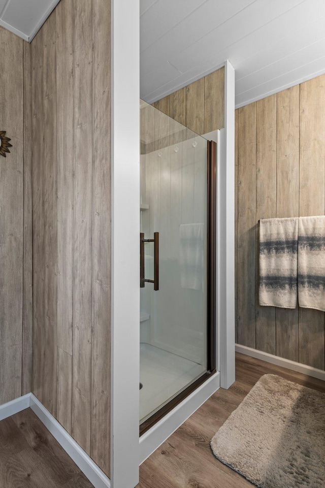 bathroom featuring wooden walls, a shower stall, and wood finished floors