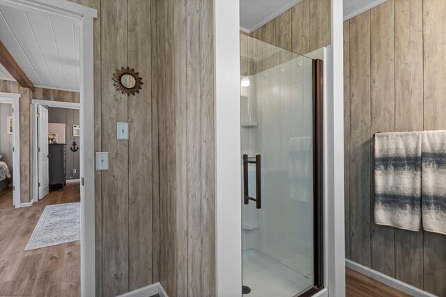 full bathroom featuring baseboards, wood walls, wood finished floors, and a stall shower