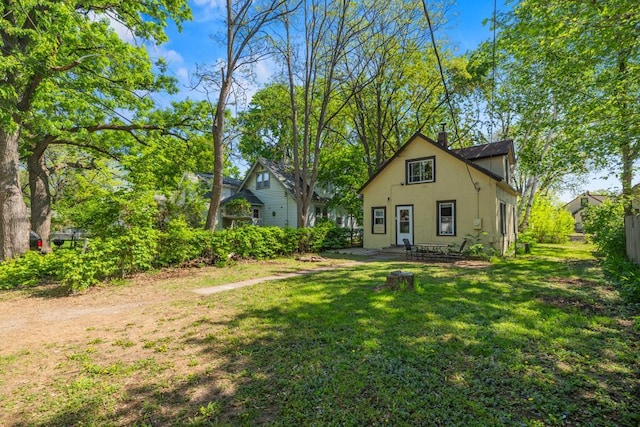 rear view of house featuring stucco siding, a lawn, and a chimney