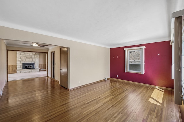 unfurnished living room with a brick fireplace, ceiling fan, baseboards, and wood finished floors