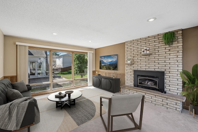 carpeted living area featuring a brick fireplace, recessed lighting, a textured ceiling, and a wainscoted wall