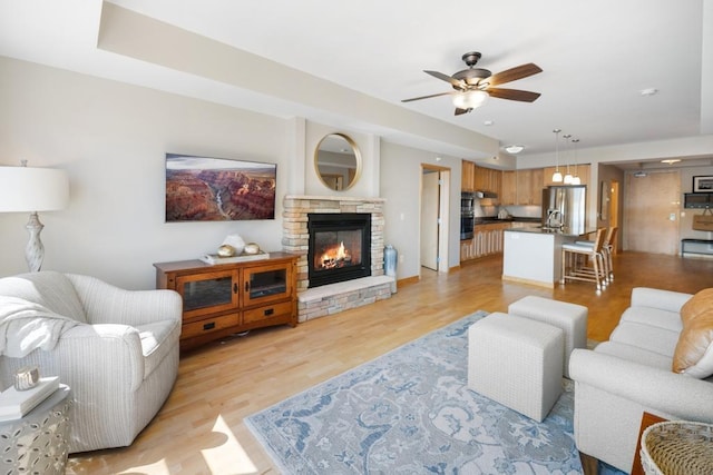 living room with ceiling fan, a stone fireplace, and light wood-style floors