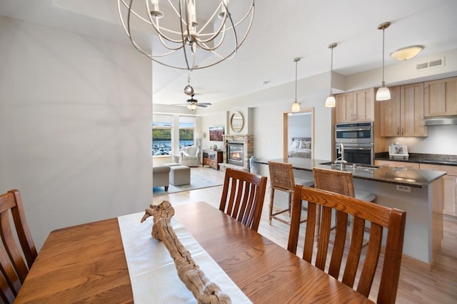 dining space featuring a stone fireplace, a chandelier, light wood-style flooring, and ceiling fan