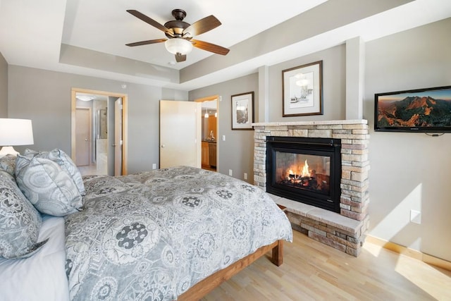 bedroom featuring a tray ceiling, baseboards, a glass covered fireplace, ceiling fan, and wood finished floors