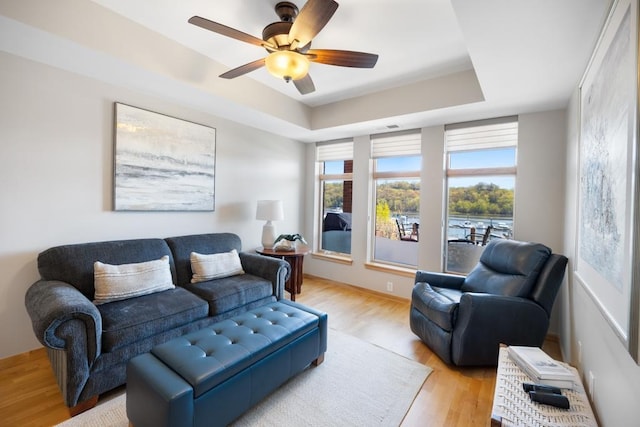 living area featuring a tray ceiling, light wood-style flooring, and a ceiling fan
