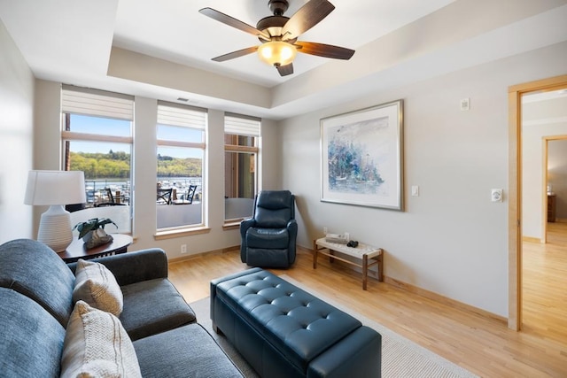 living room with baseboards, a raised ceiling, light wood-style floors, and ceiling fan