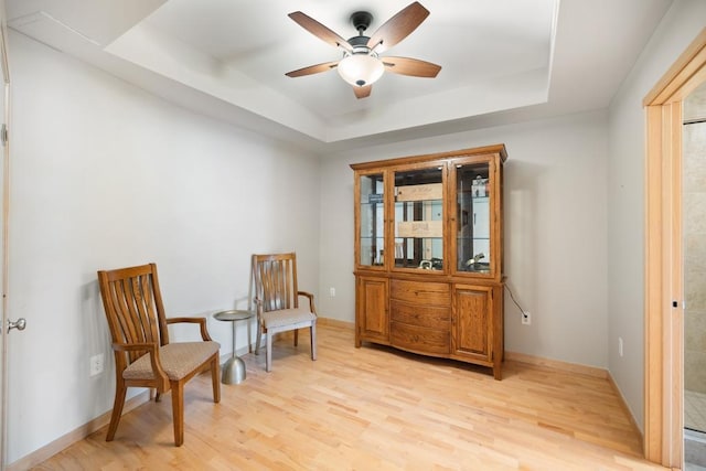living area with light wood-type flooring, a raised ceiling, baseboards, and ceiling fan