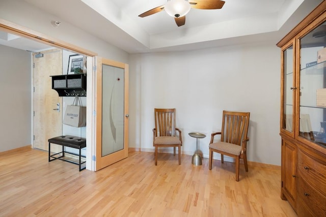 sitting room with a tray ceiling, light wood-style floors, ceiling fan, and baseboards
