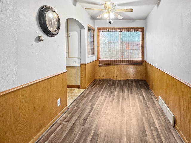 empty room with wood finished floors, visible vents, ceiling fan, and a wainscoted wall
