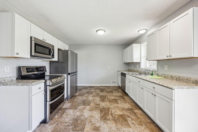 8040 Xenia Ave N, Brooklyn Park, MN 55443 - kitchen with appliances with stainless steel finishes, a sink, white cabinets, baseboards, and stone finish floors