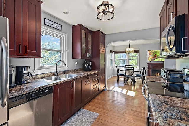 kitchen featuring stainless steel appliances, a sink, arched walkways, light wood-style floors, and a warm lit fireplace