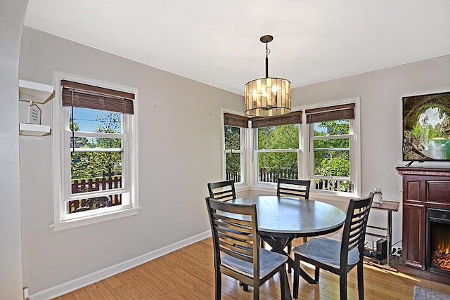 dining space with light wood-style flooring, a chandelier, baseboards, and a warm lit fireplace