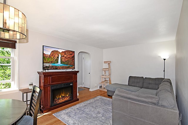 living area featuring wood finished floors, arched walkways, and a lit fireplace
