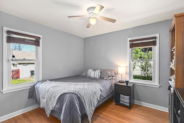 bedroom with multiple windows, light wood-style floors, and baseboards