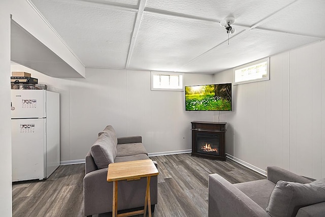 living area with dark wood-type flooring, a glass covered fireplace, a textured ceiling, and baseboards