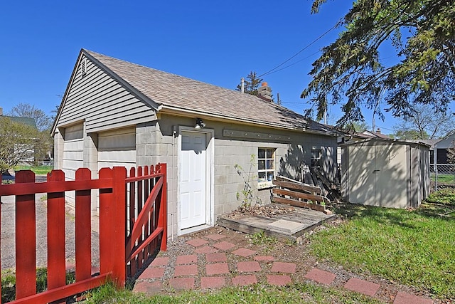 rear view of house with a shingled roof, an outbuilding, fence, and a garage