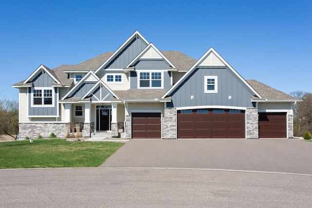 craftsman house with a front lawn, stone siding, roof with shingles, board and batten siding, and driveway