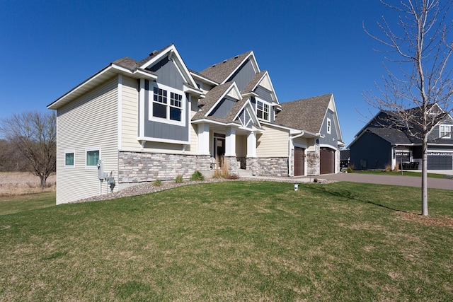 craftsman-style house featuring a front yard, driveway, an attached garage, and stone siding