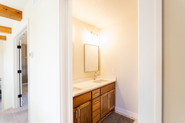 bathroom with double vanity, a sink, baseboards, and beam ceiling