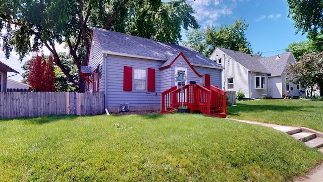 bungalow-style house featuring fence, roof with shingles, and a front lawn