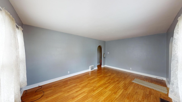 unfurnished room featuring visible vents, arched walkways, baseboards, and wood finished floors