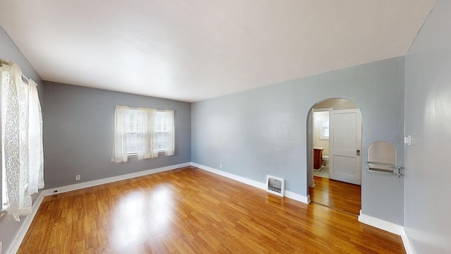 spare room with arched walkways, baseboards, wood finished floors, and visible vents