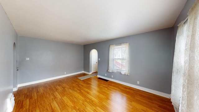 interior space featuring light wood-type flooring, arched walkways, baseboards, and visible vents