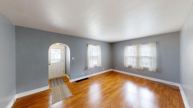 entrance foyer featuring arched walkways, baseboards, wood finished floors, and visible vents