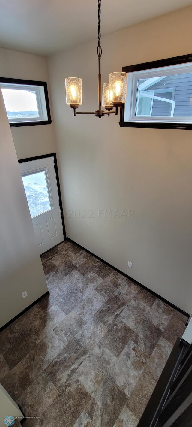 entryway featuring baseboards, a notable chandelier, and stone finish floor