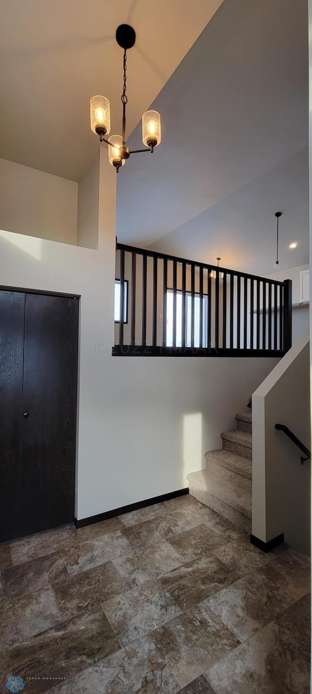 stairs featuring an inviting chandelier, stone finish floor, lofted ceiling, and baseboards