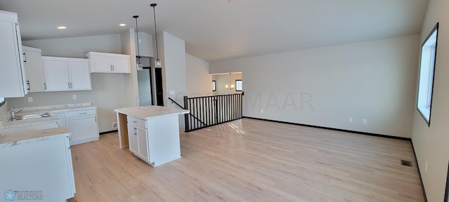 kitchen with a sink, light wood-style floors, visible vents, white cabinetry, and lofted ceiling