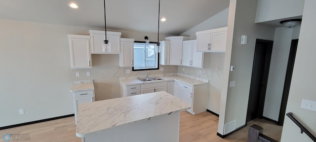 kitchen with white cabinetry, a sink, a kitchen island, light wood finished floors, and vaulted ceiling