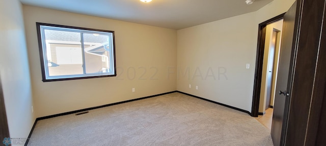 spare room featuring visible vents, light colored carpet, and baseboards