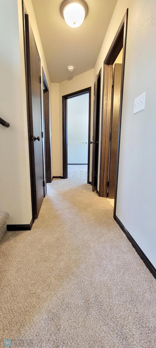 hallway featuring light colored carpet and baseboards