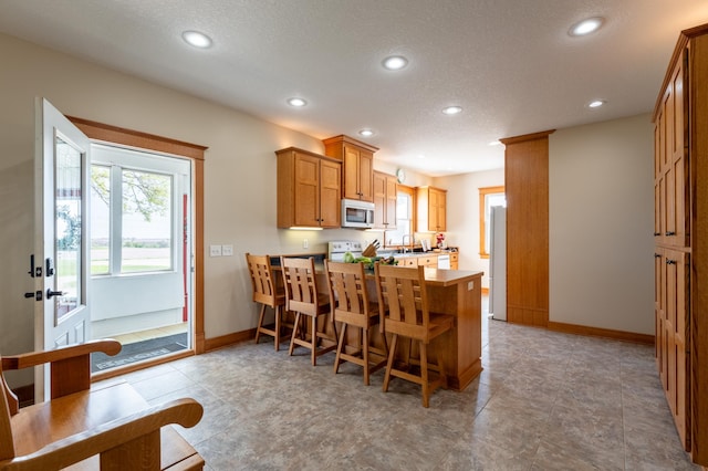 kitchen with white appliances, a peninsula, recessed lighting, baseboards, and a kitchen breakfast bar