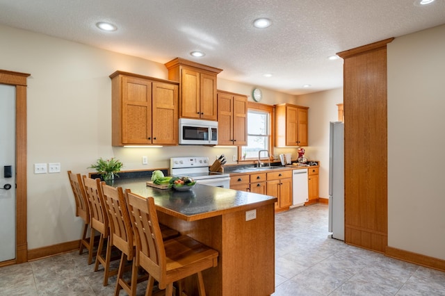 kitchen with white appliances, a peninsula, a sink, baseboards, and a textured ceiling
