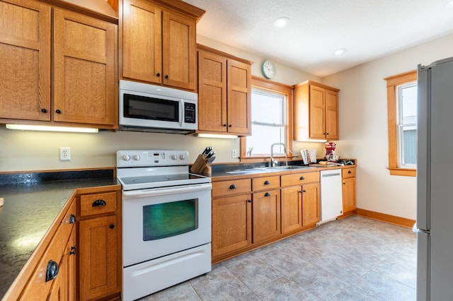 kitchen featuring white appliances, a sink, dark countertops, recessed lighting, and brown cabinets