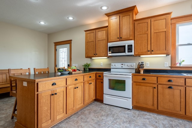 kitchen with white appliances, a peninsula, dark countertops, brown cabinets, and a kitchen bar