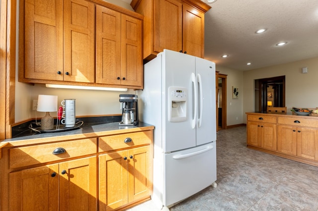 kitchen featuring white refrigerator with ice dispenser, recessed lighting, brown cabinets, baseboards, and a textured ceiling