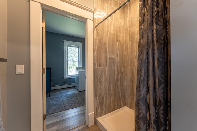 full bathroom with a stall shower, baseboard heating, washer / dryer, and wood finished floors